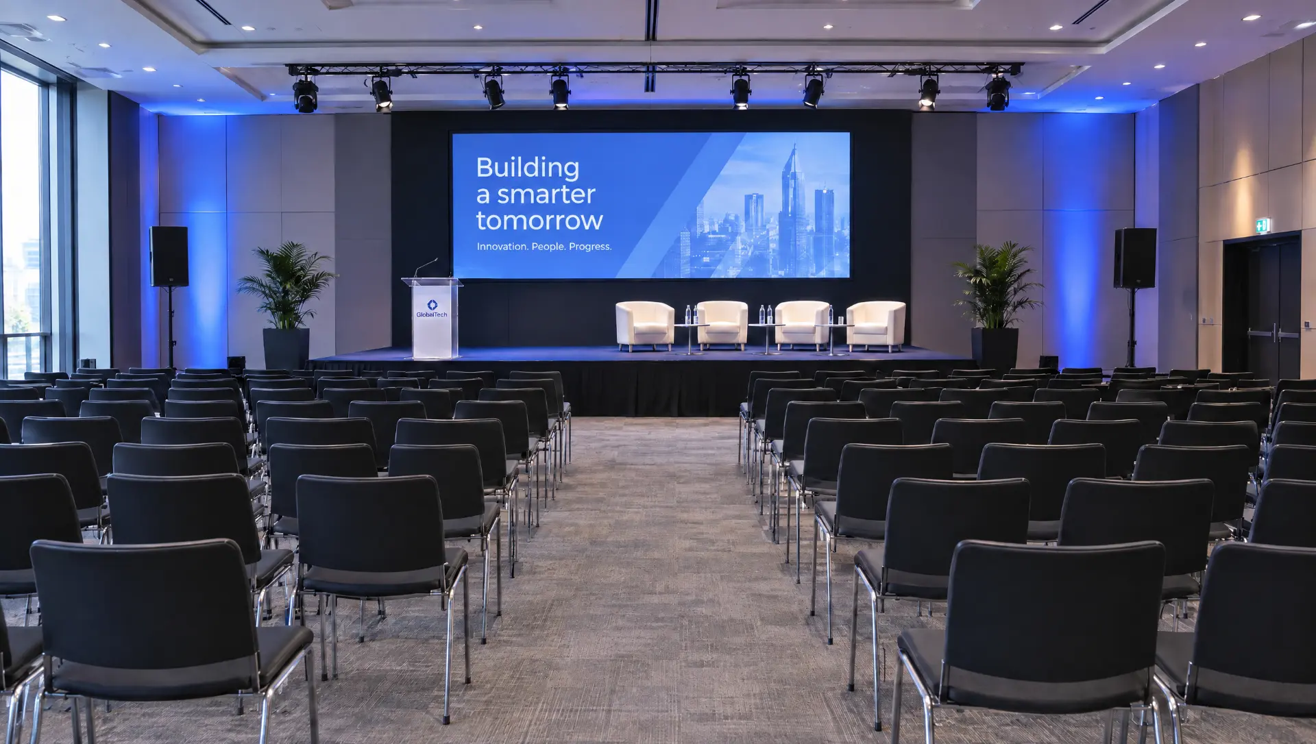 Corporate event hall with a lit stage, presentation screen and rows of chairs ready for guests